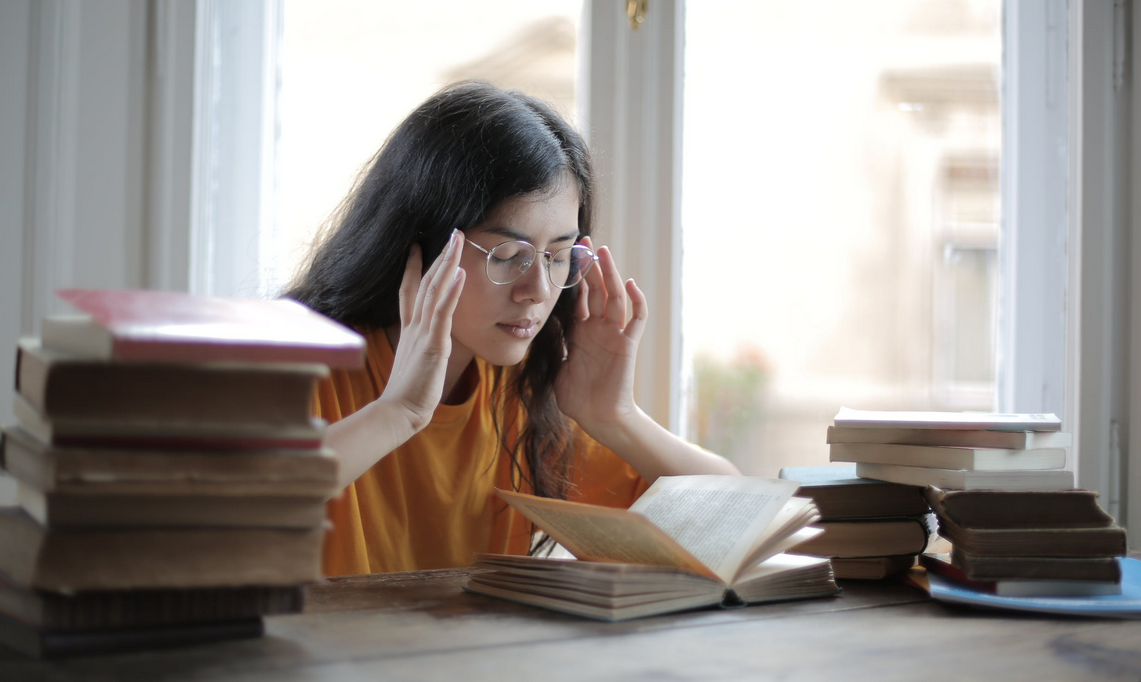 student touching her head with books on the table
